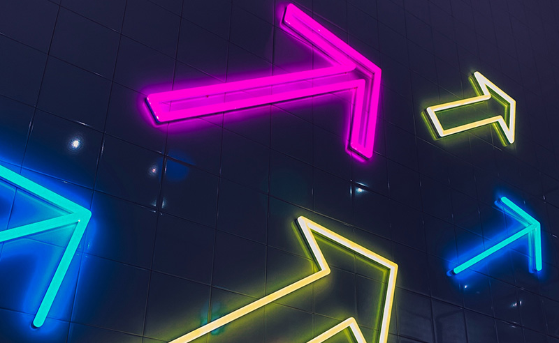 neon arrows pointing towards the right hand corner of a dark wall