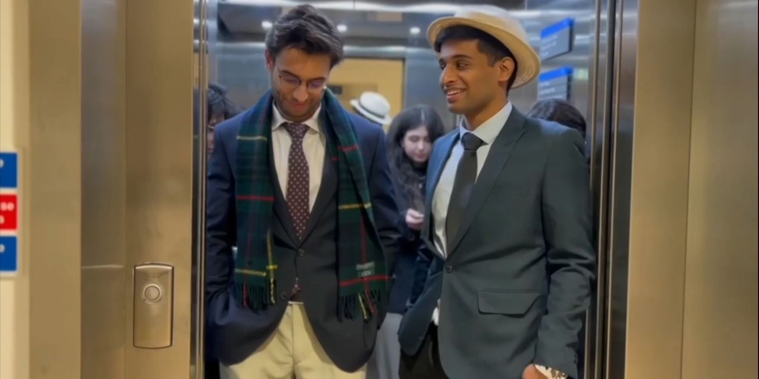 Two well dressed men stand at the front of an elevator, the doors about to close.