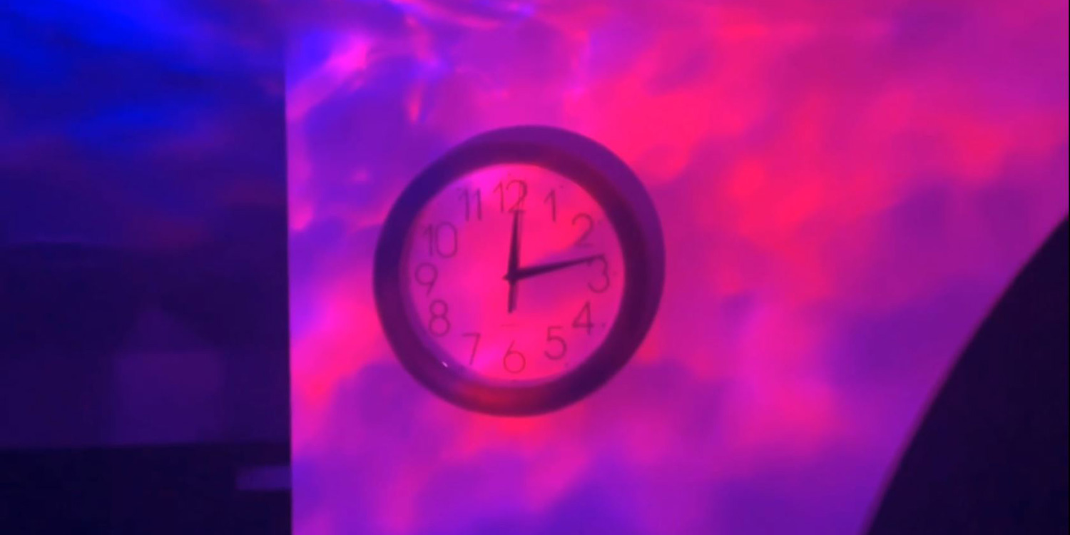 An analogue clock shows 12:15, dappled in a purple strobe light.