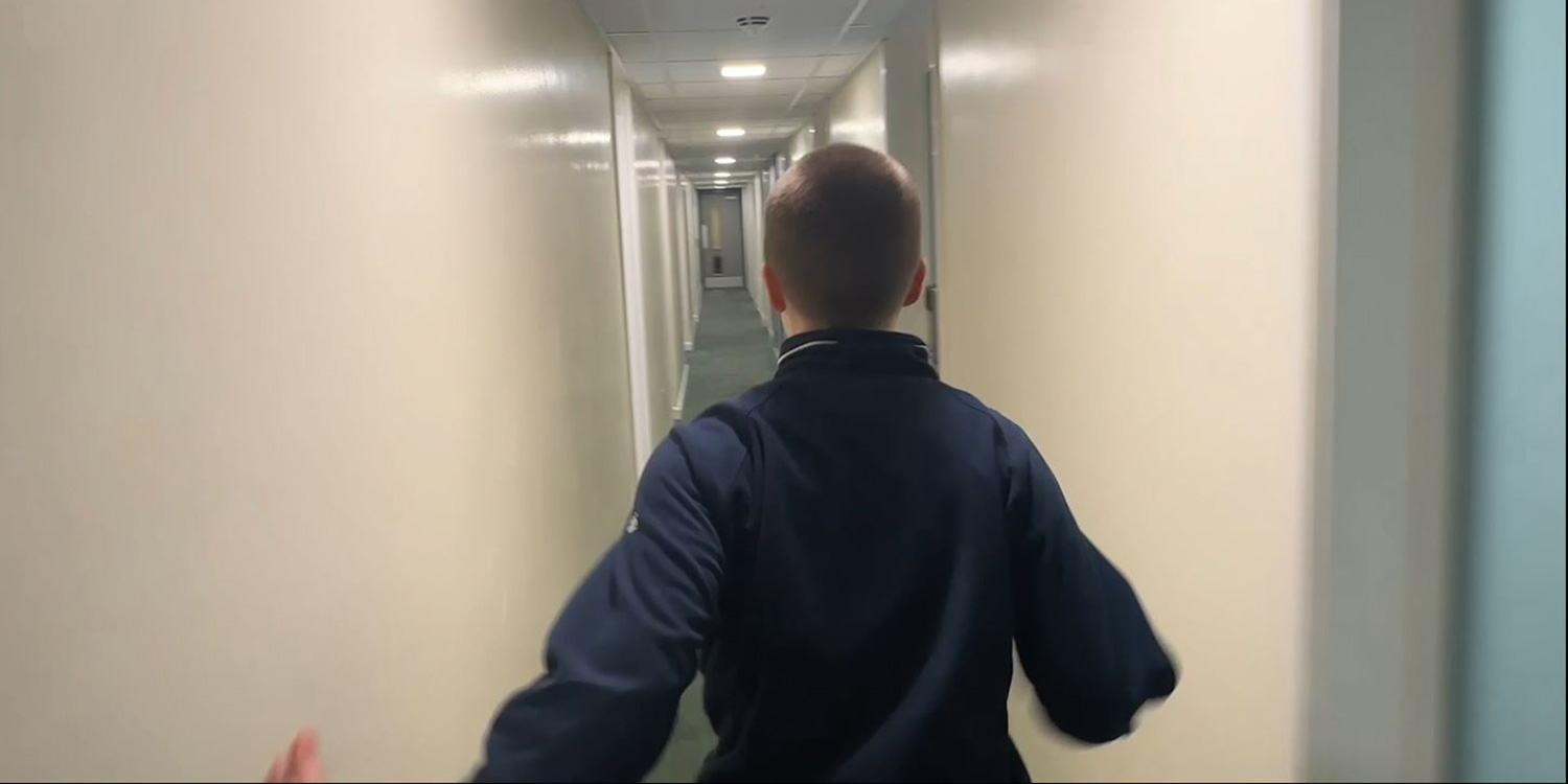 A boy faces away from the camera, running down a narrow corridor.