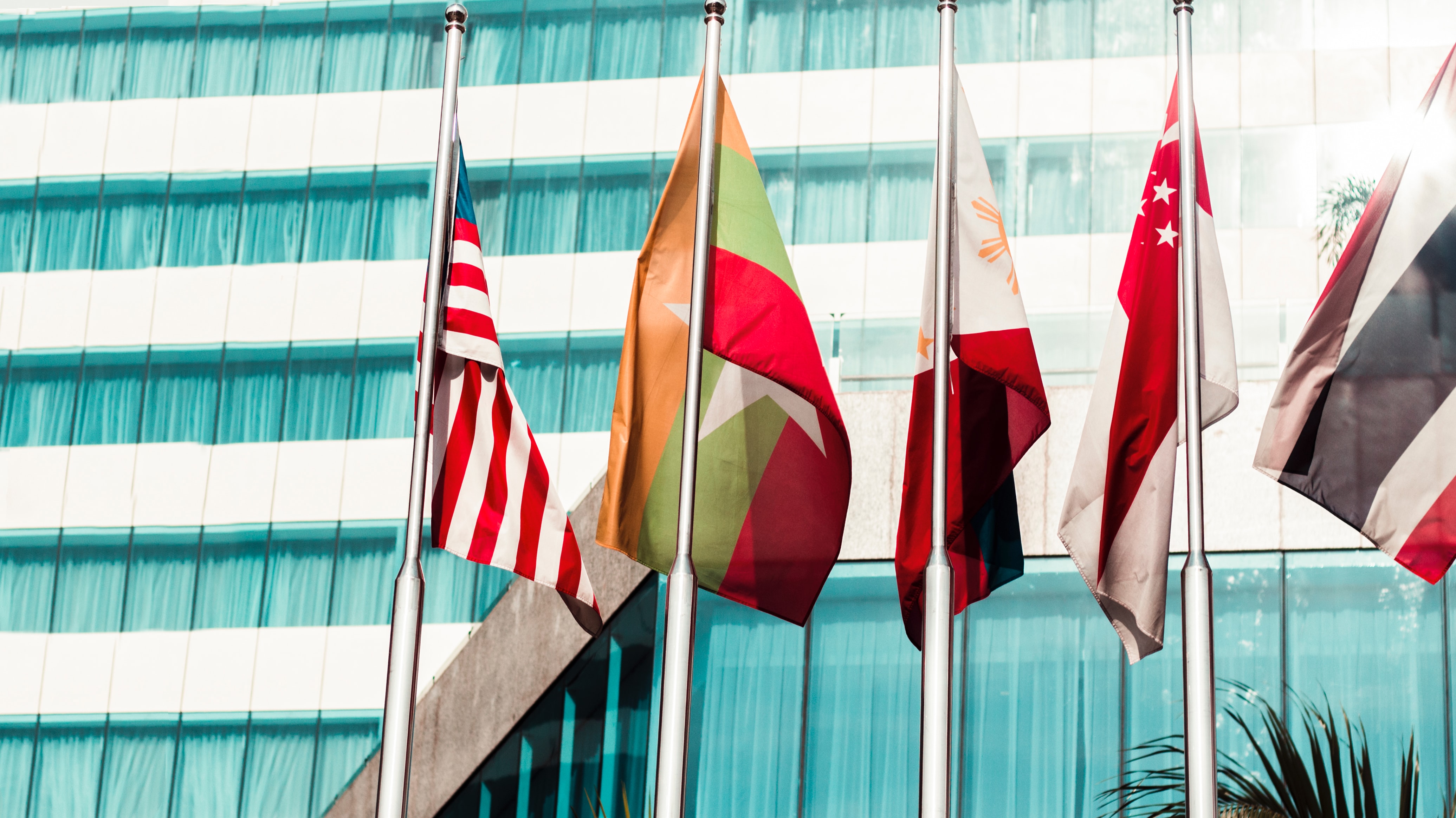 Several Flags outside a blue-windowed building hanging in gentle wind