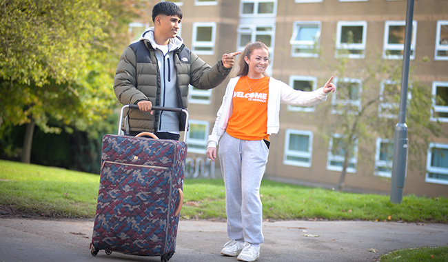 A student ambassador helps a new student with their suitcase