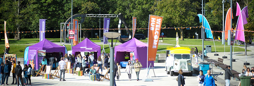 The Welcome Hub on the Piazza in the sunshine bedecked with festival flags and gazebos