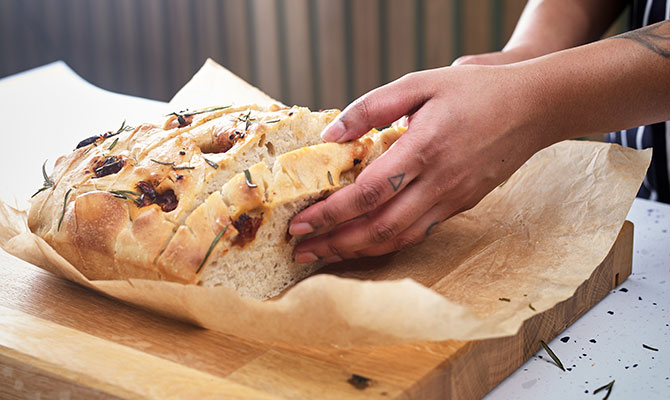 Hand cooked foccacia being sliced on a wooden chopping board