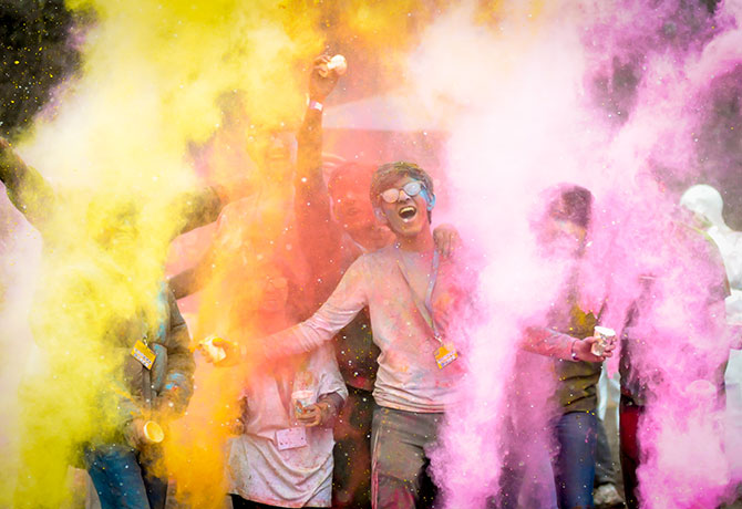 A student roars in excitement as Holi colour powder surrounds them