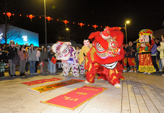 Lion Dancers in full costume on the Piazza dancing to a crowd underneath lantern lighting