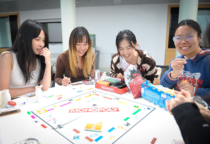 A group of students laugh and munch on snacks as they play monopoly