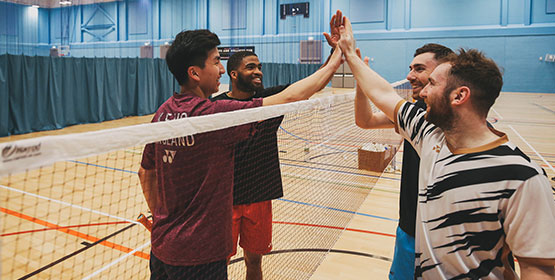 A group of players high five each other over the badminton net