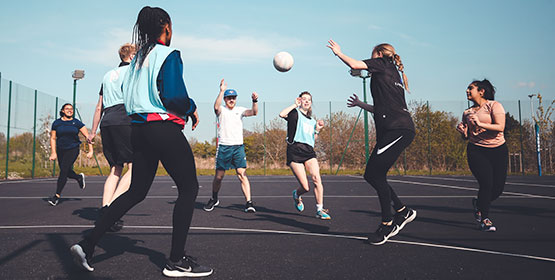 A group of Netball players in action, caught mid-shot jumping for the ball.