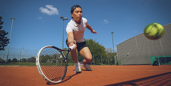 A tennis player reaching for the shot, racket out stretched against a clear blue sky.