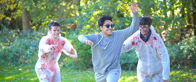 A student laughs as they run away from two more students dressed up as zombies