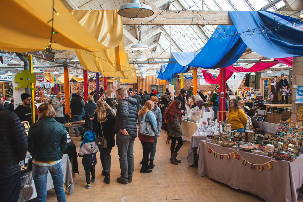 The brightly coloured market pictured is a buzz with people and activity. Blue and yellow canvas are draped over the joists of the building making the place feel alive and busy