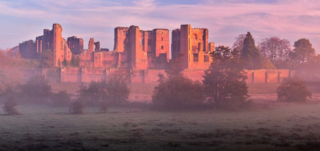 A stone castle, half in ruins, sits amongst the trees and mist of Kenilworth.