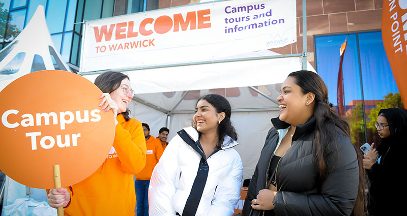 Two new students smile as they embark with a current student on a tour