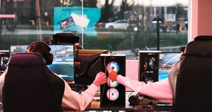 Two students fist-bump whilst playing videogames on two PCs side-by-side.