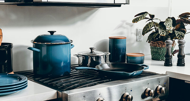 A set of pans on the stove in the kitchen and plates stacked neatly to the side.