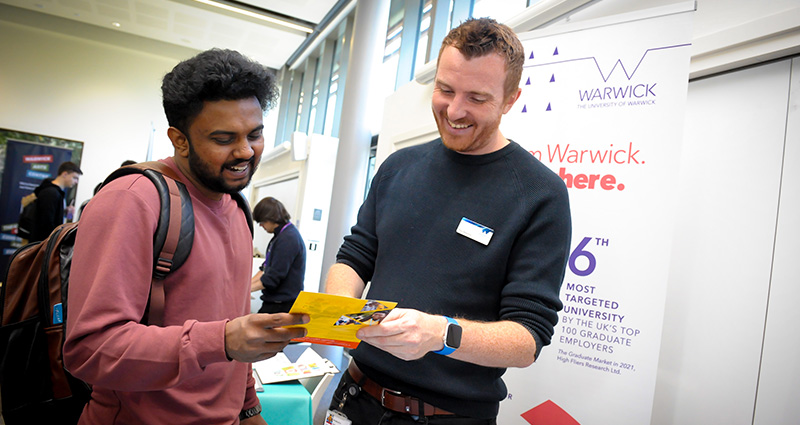 A member of staff smiles as they explain a leaflet to a new student