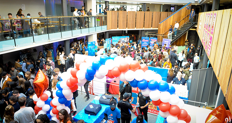 The SU Welcome fair in full swing, crowds of people fill the room with a giant balloon arch on display.