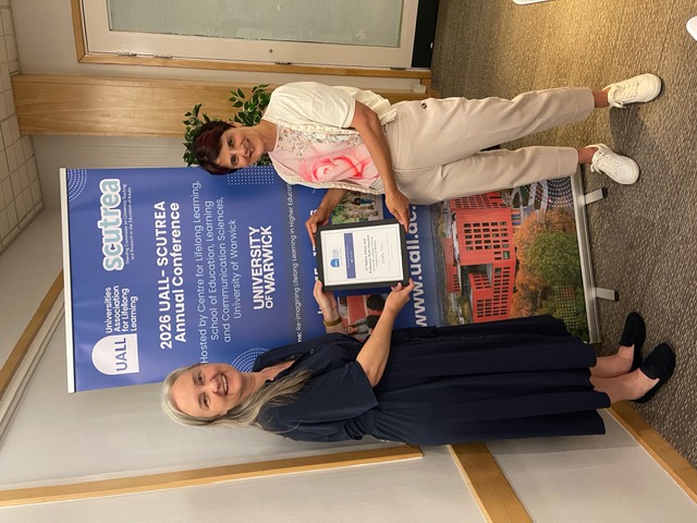 Nalita and Ruth hosting an award certificate in front of the conference banner