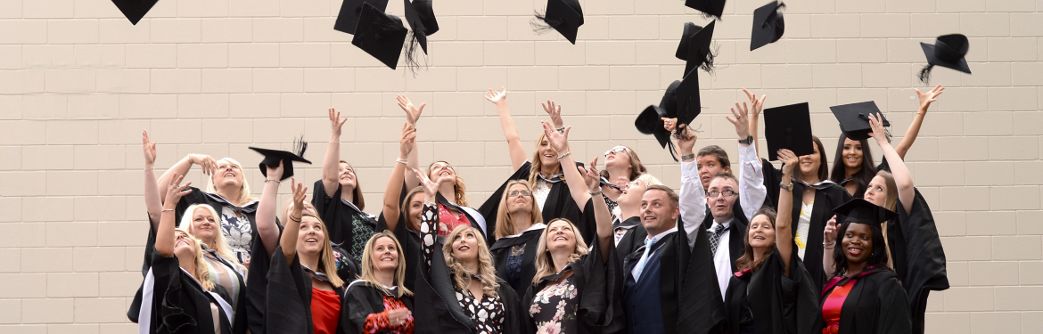 a group of cll alumni wearing graduate gown throwing their hats into the sky