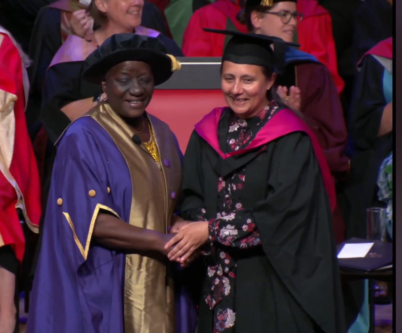 Mia in graduation gown on the right shaking hands with a chancellor on the left