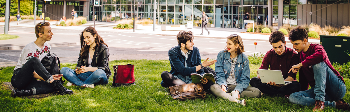 A group of students sitting on the grass on campus chatting