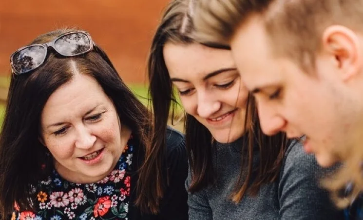 Three students looking down at something and smiling