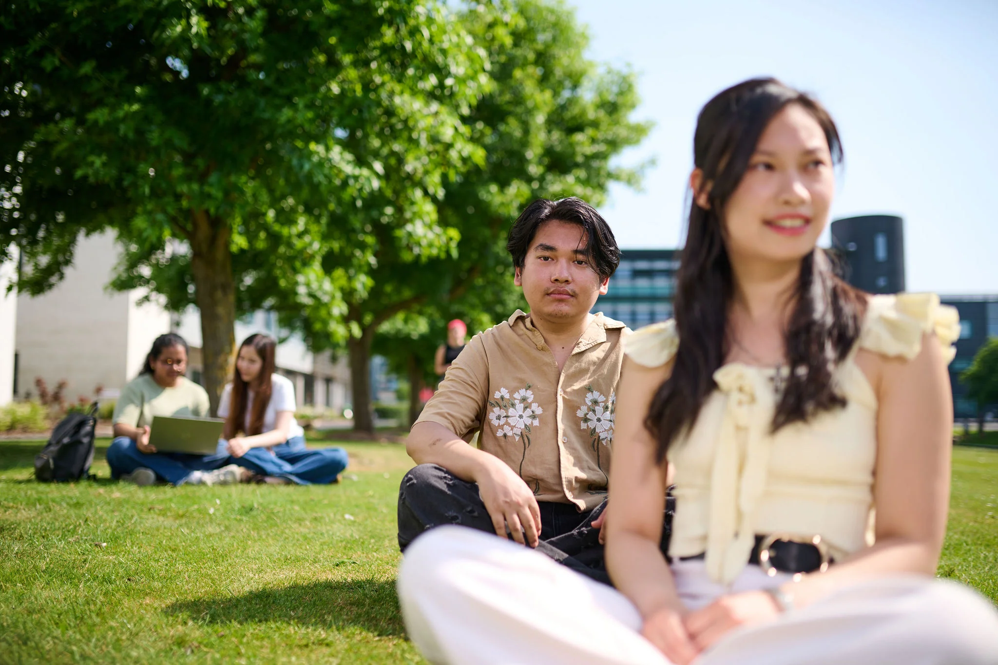 Two students are sitting on a grassy area on campus.
