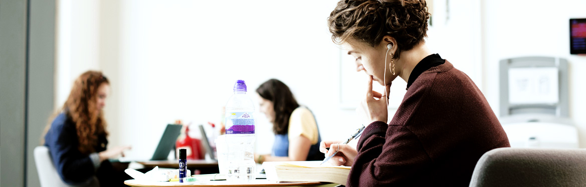 A student in the Oculus Building on campus reading from a textbook.