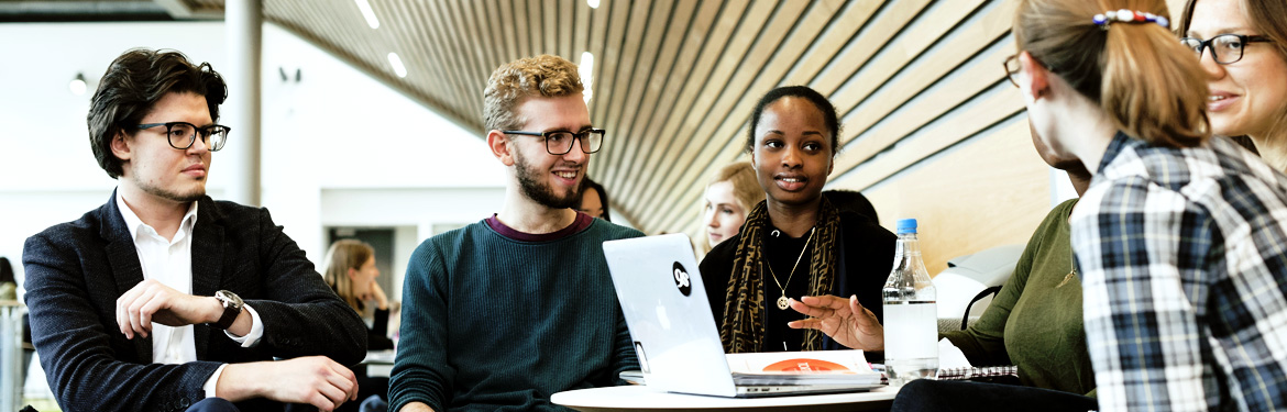 Image of economics students in conversation around a desk.