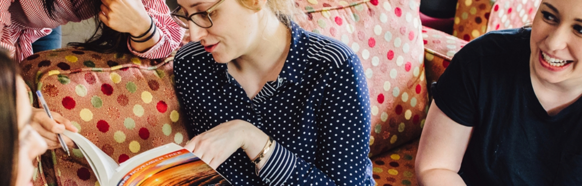 This image shows a female a student sitting on a polka-dot sofa reading a book with several others