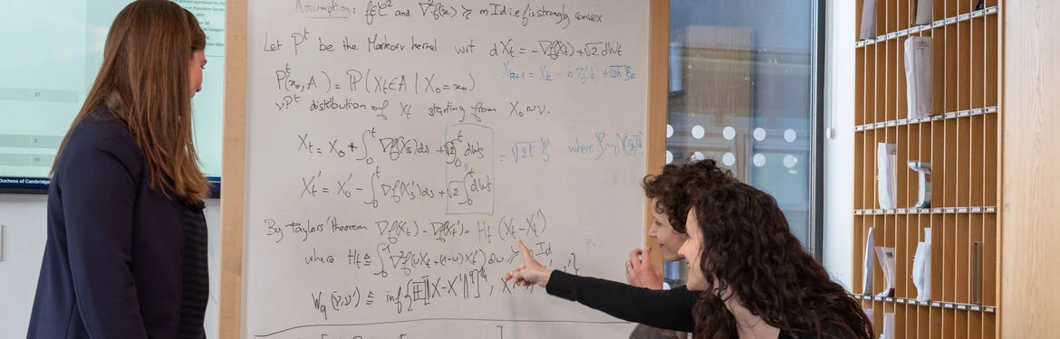 Three students discuss mathematical equations on a whiteboard.