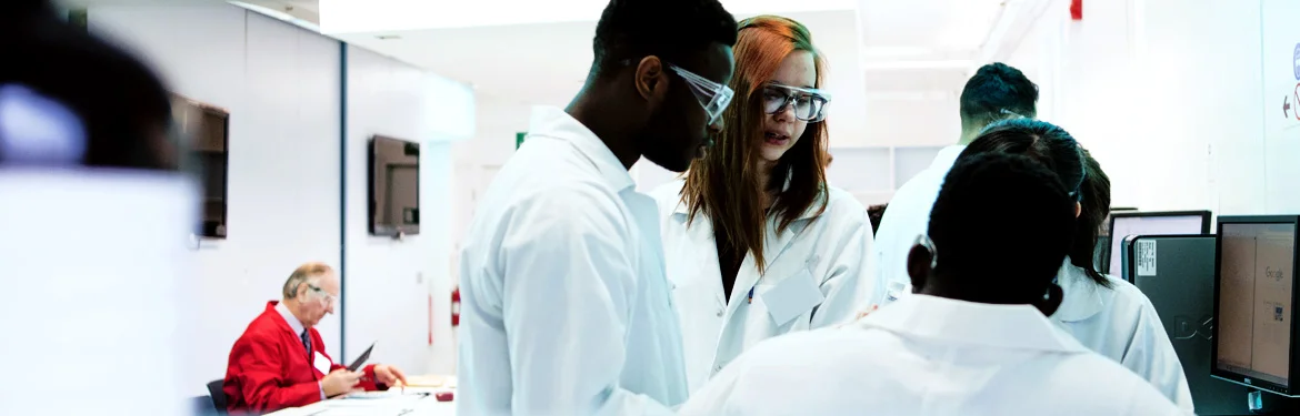 Students in lab coats and safety goggles collaborating in a laboratory.