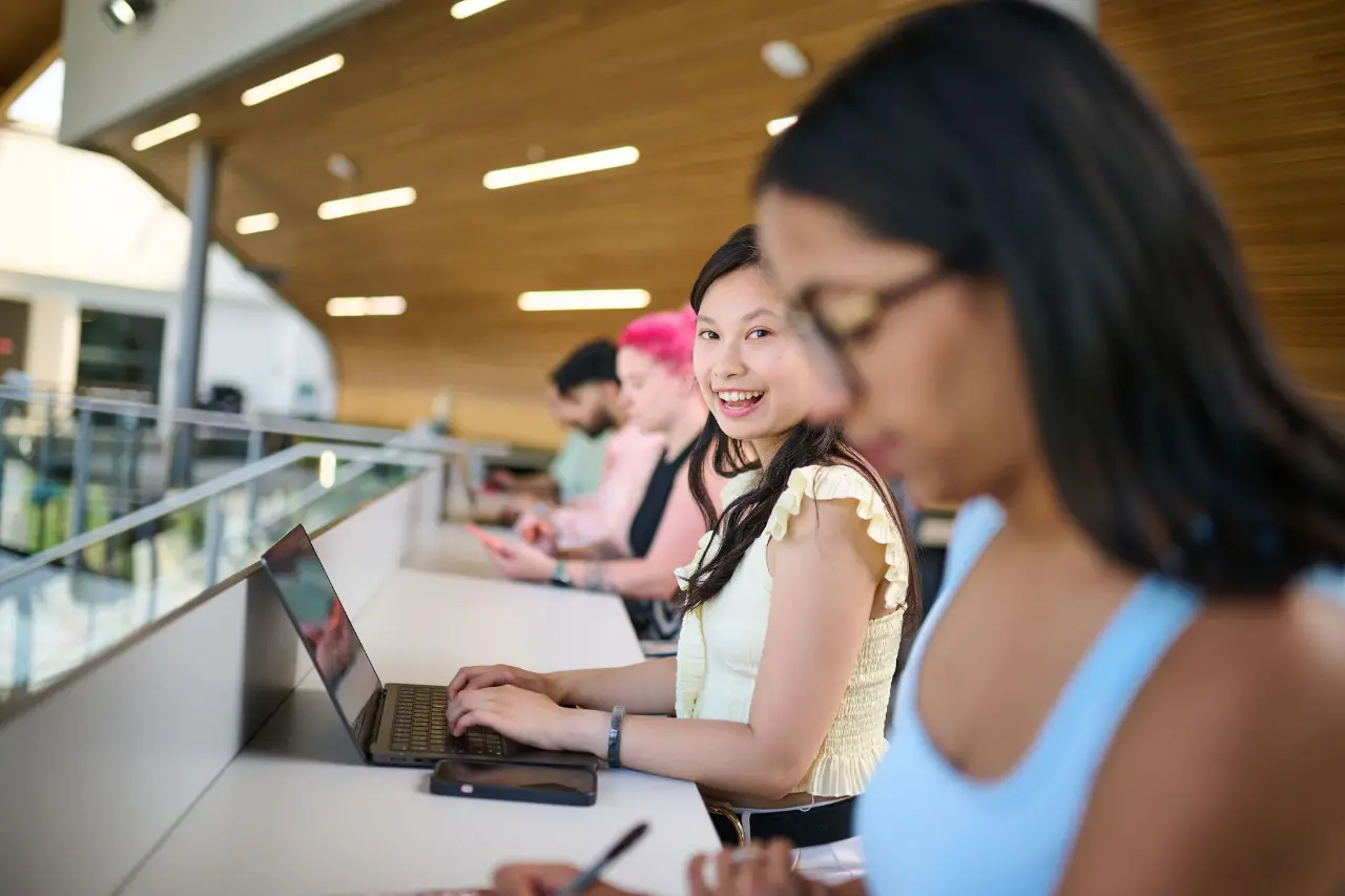 A student sits at a table working on a laptop and wearing headphones.