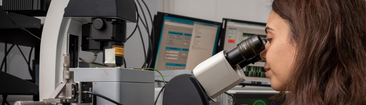 Woman looks through a microscope to examine a sample