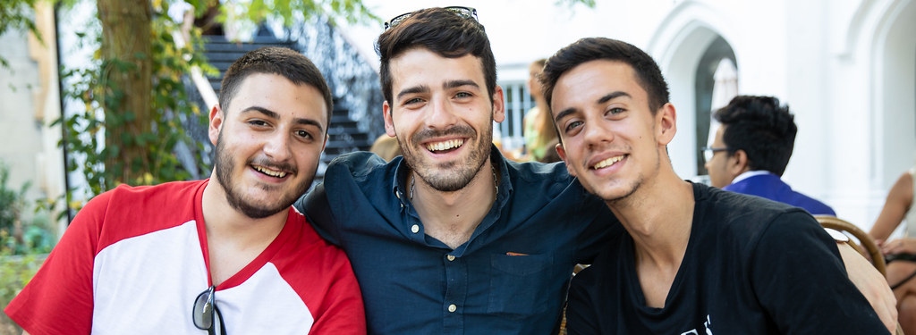 three male students sitting outside together