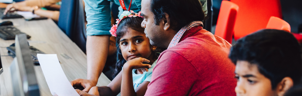 children and family sitting in front of computers in a campus event