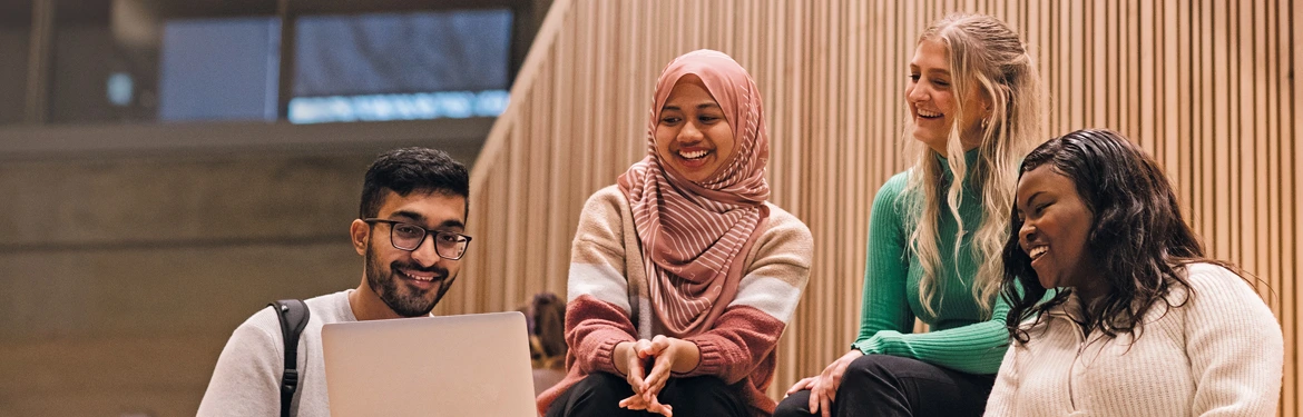 A group of International Business and Management undergraduate students sitting around a laptop and smiling