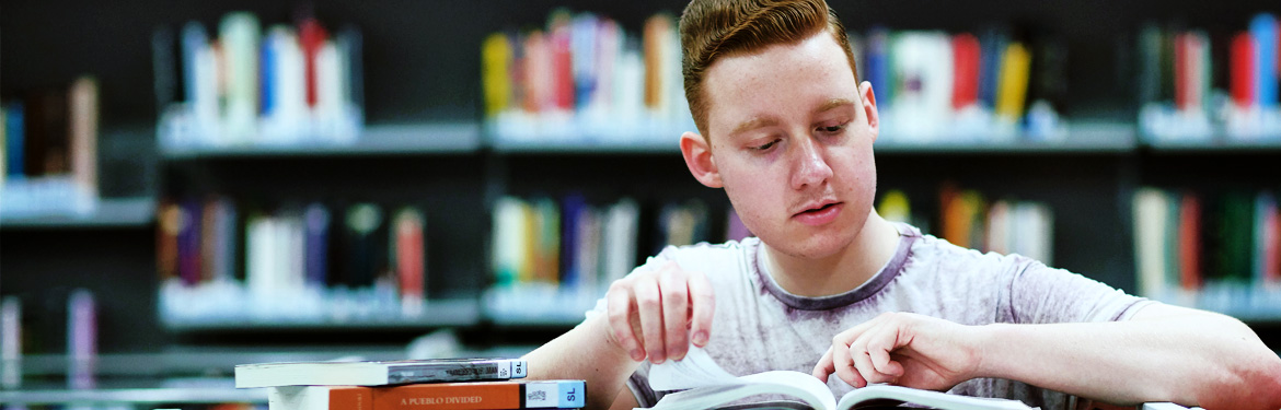 This image shows a young male student studying in a library on campus