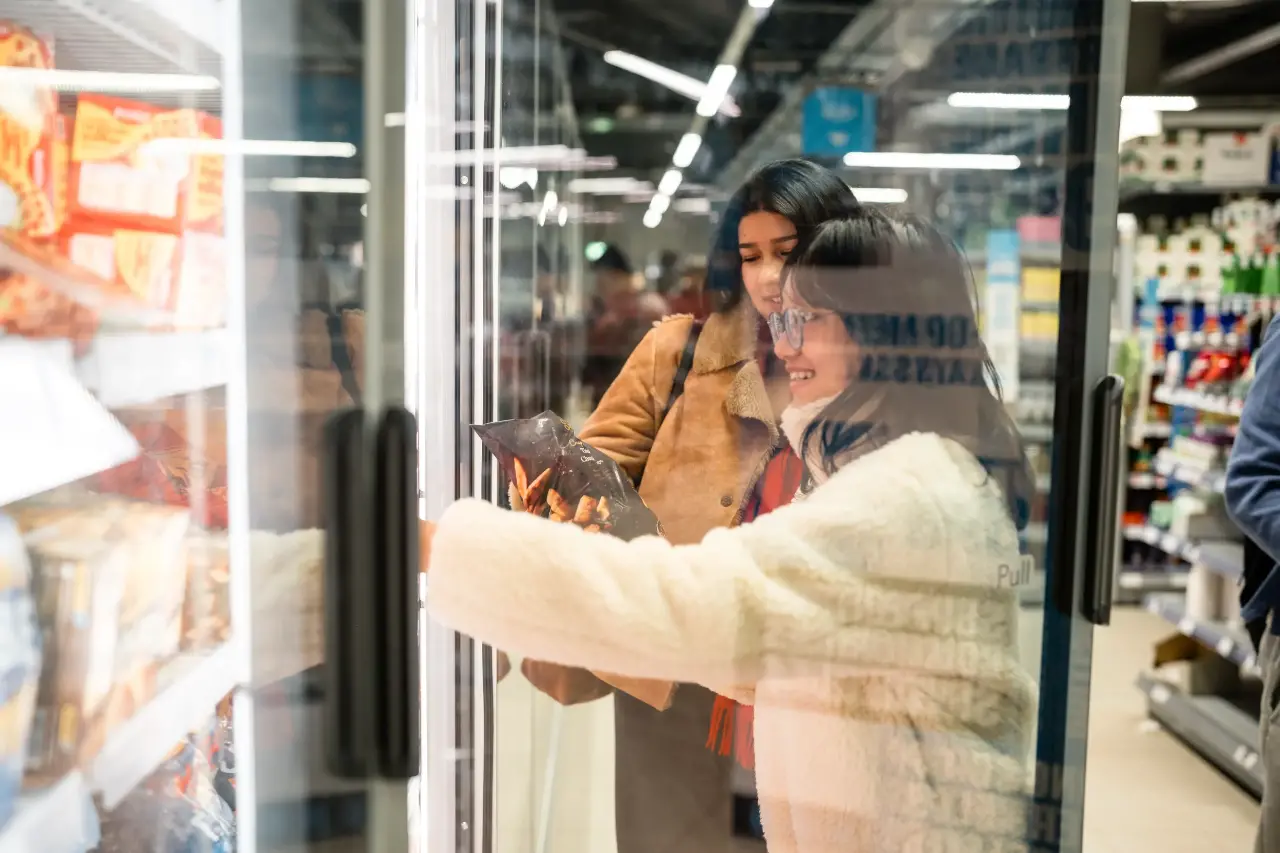 Two students shopping in the freezer section of a supermarket.