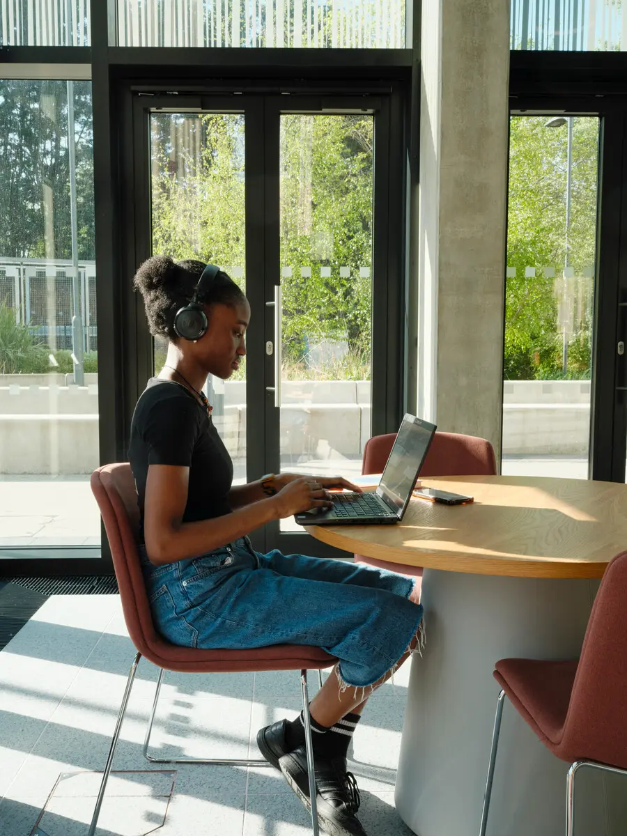 A student sits at a table working on a laptop and wearing headphones.