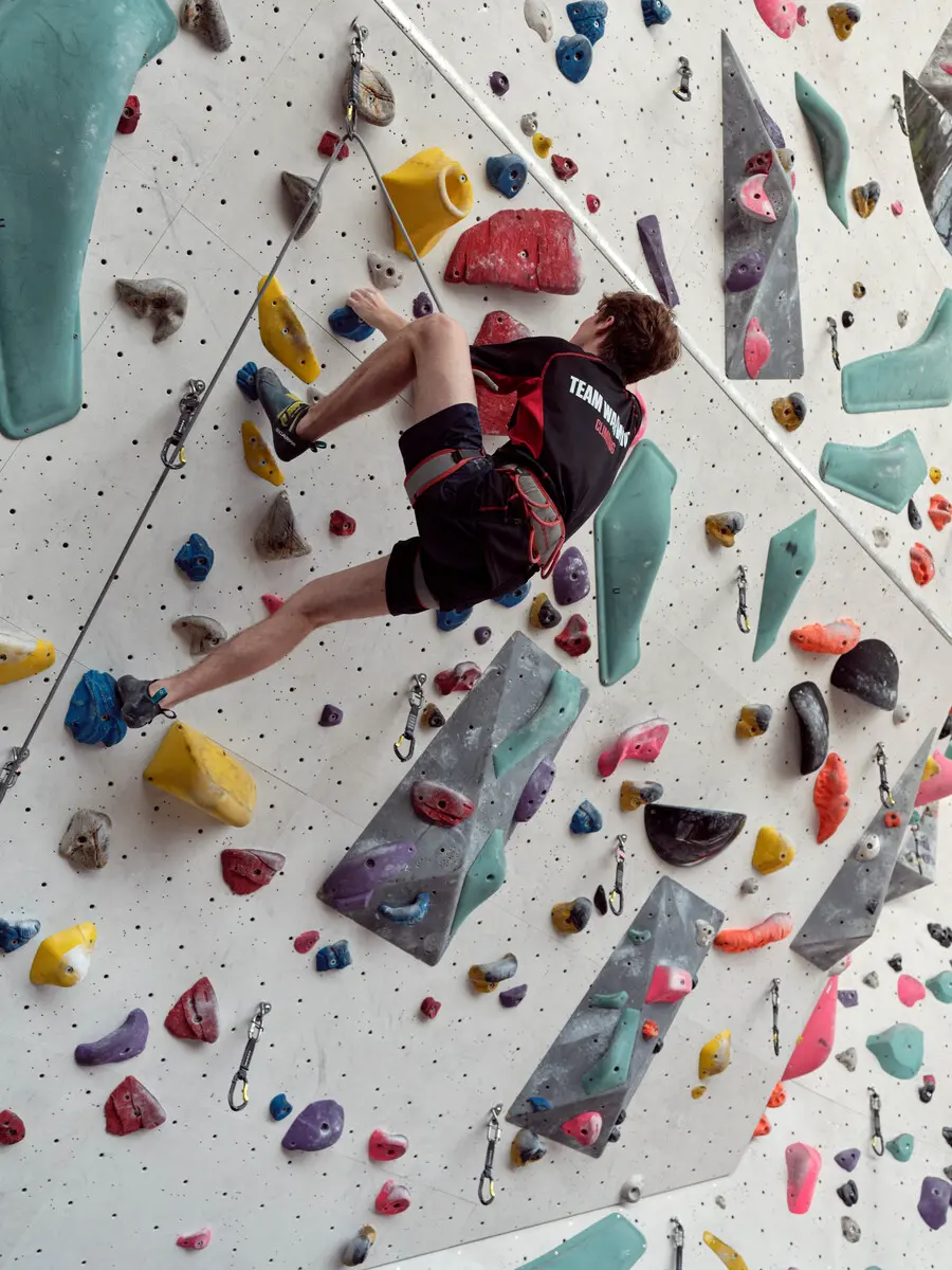 A student in a sports top is scaling a climbing wall.