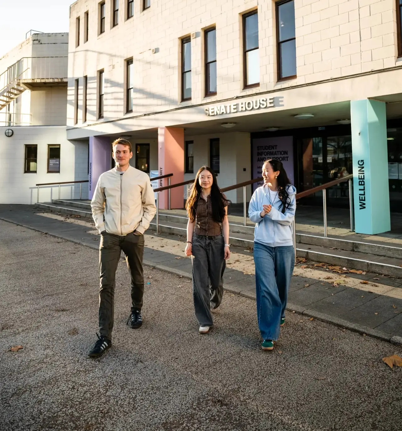 Three students walking in front of a campus building.