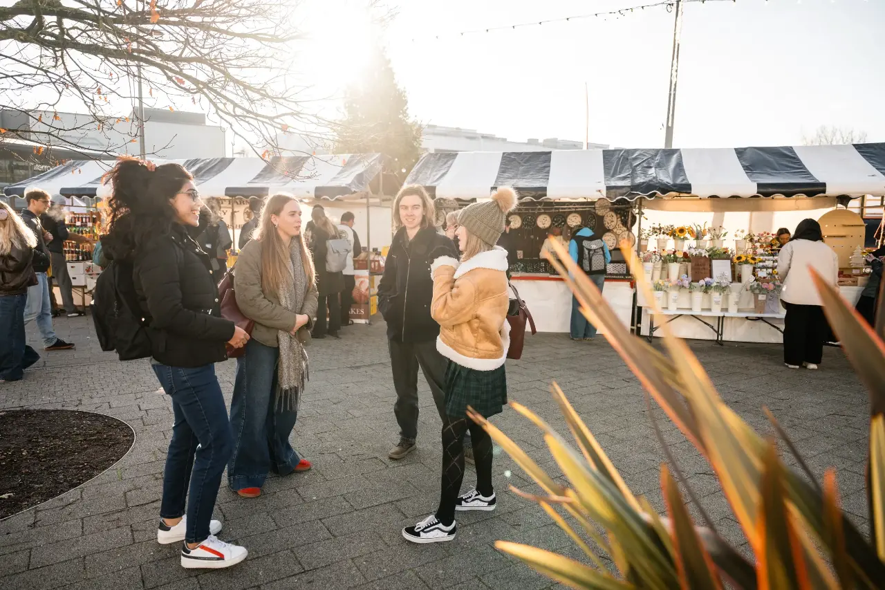 A group of students are standing in front of a busy market happily chatting.