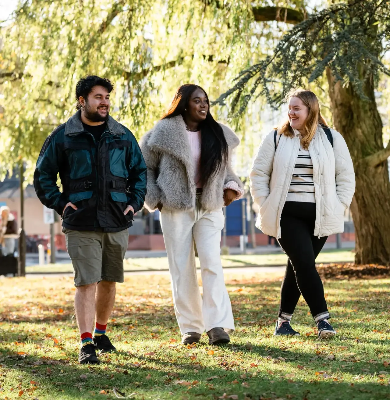 Three students walking through a sunny, green campus.