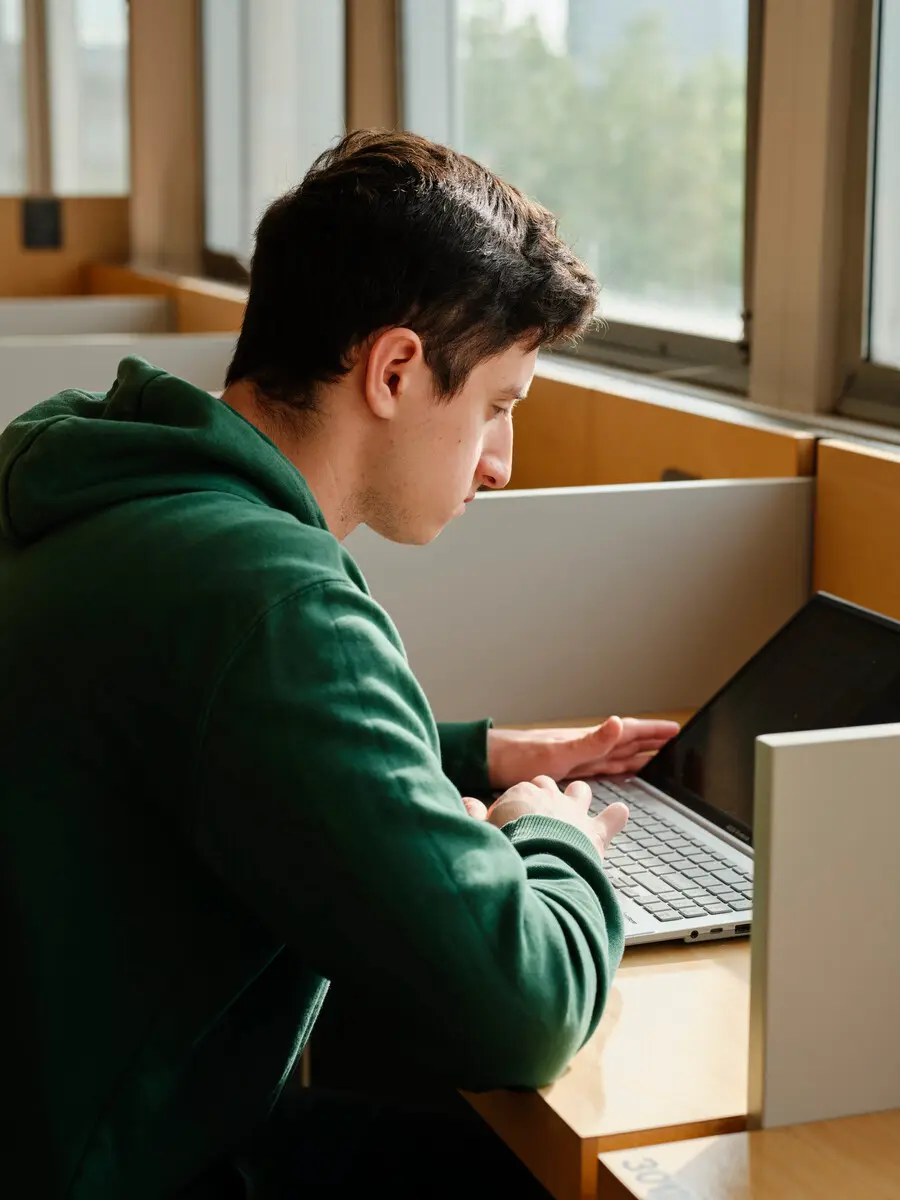 A student in a green jumper using a laptop in a study area.