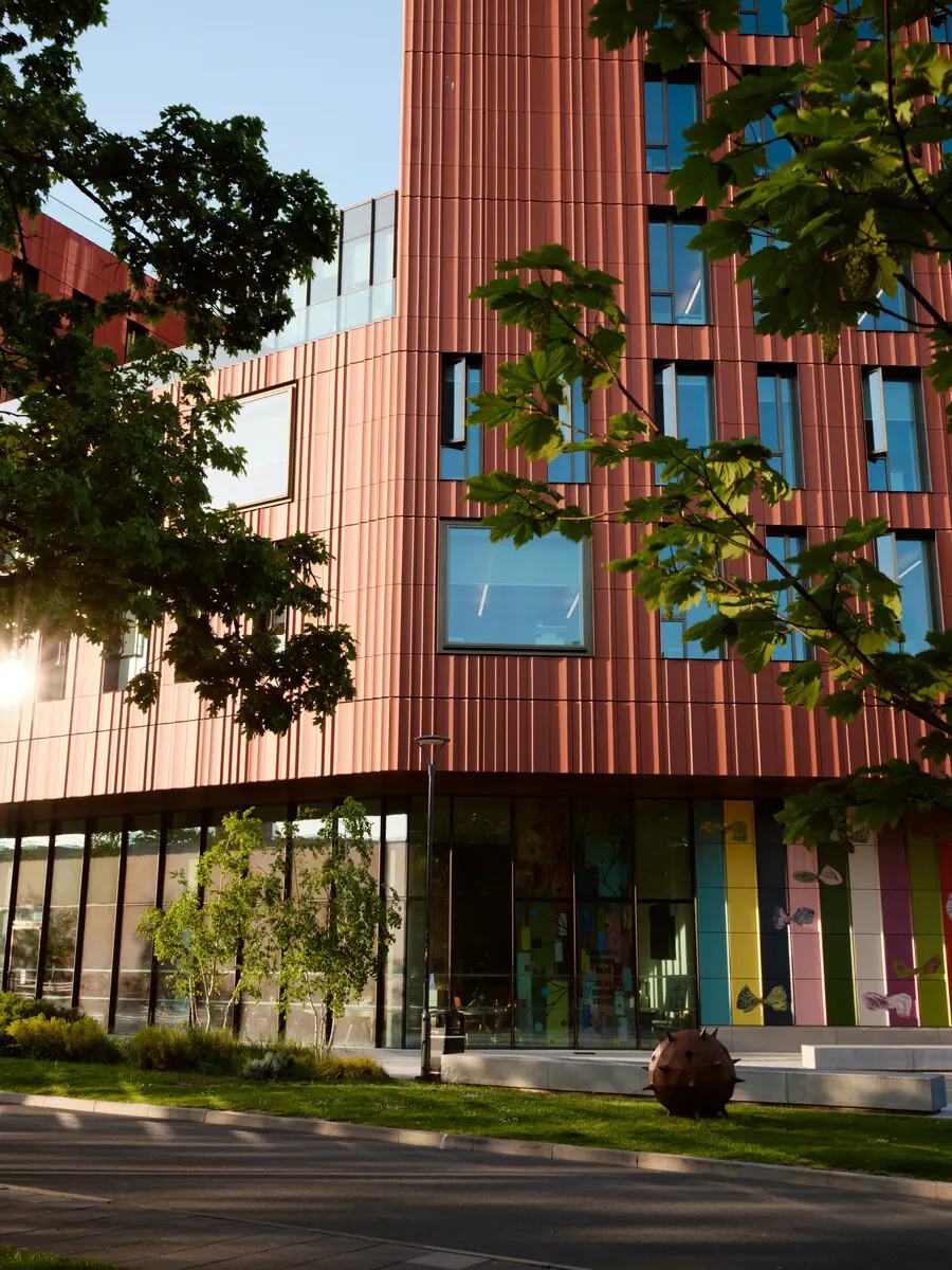 The outside of a colourful university building, surrounded by trees.