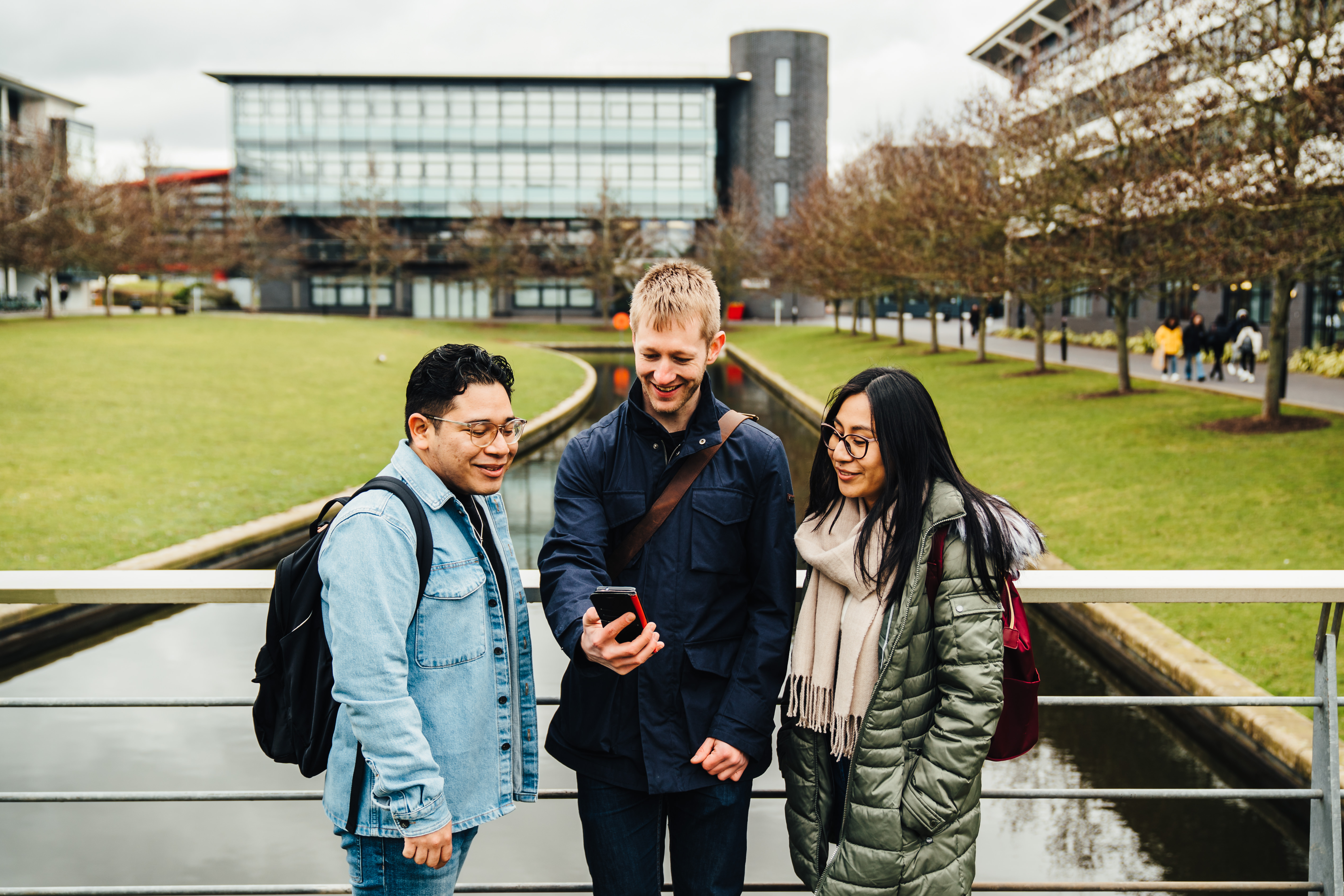 3 students reading something on their phones on campus