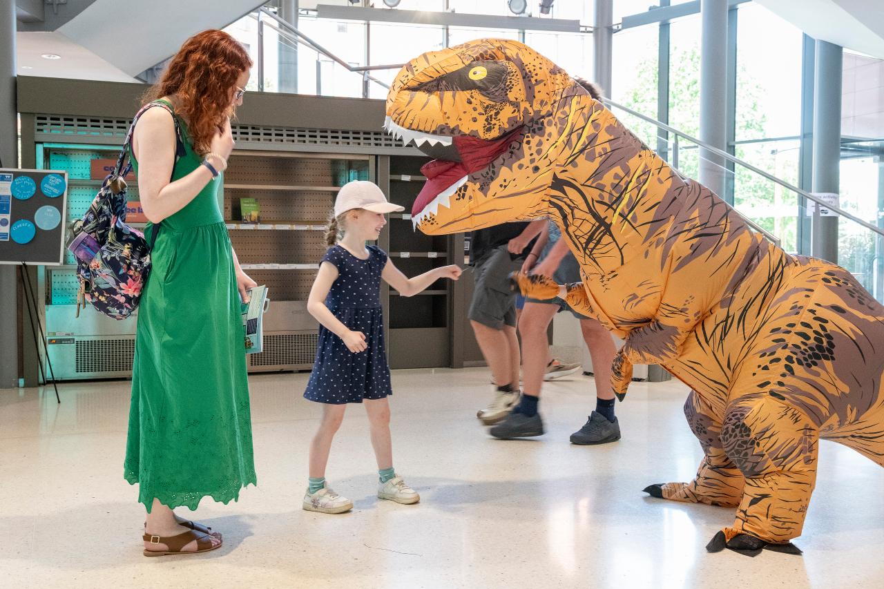 Adult and child interacting with person in dinosaur costume 