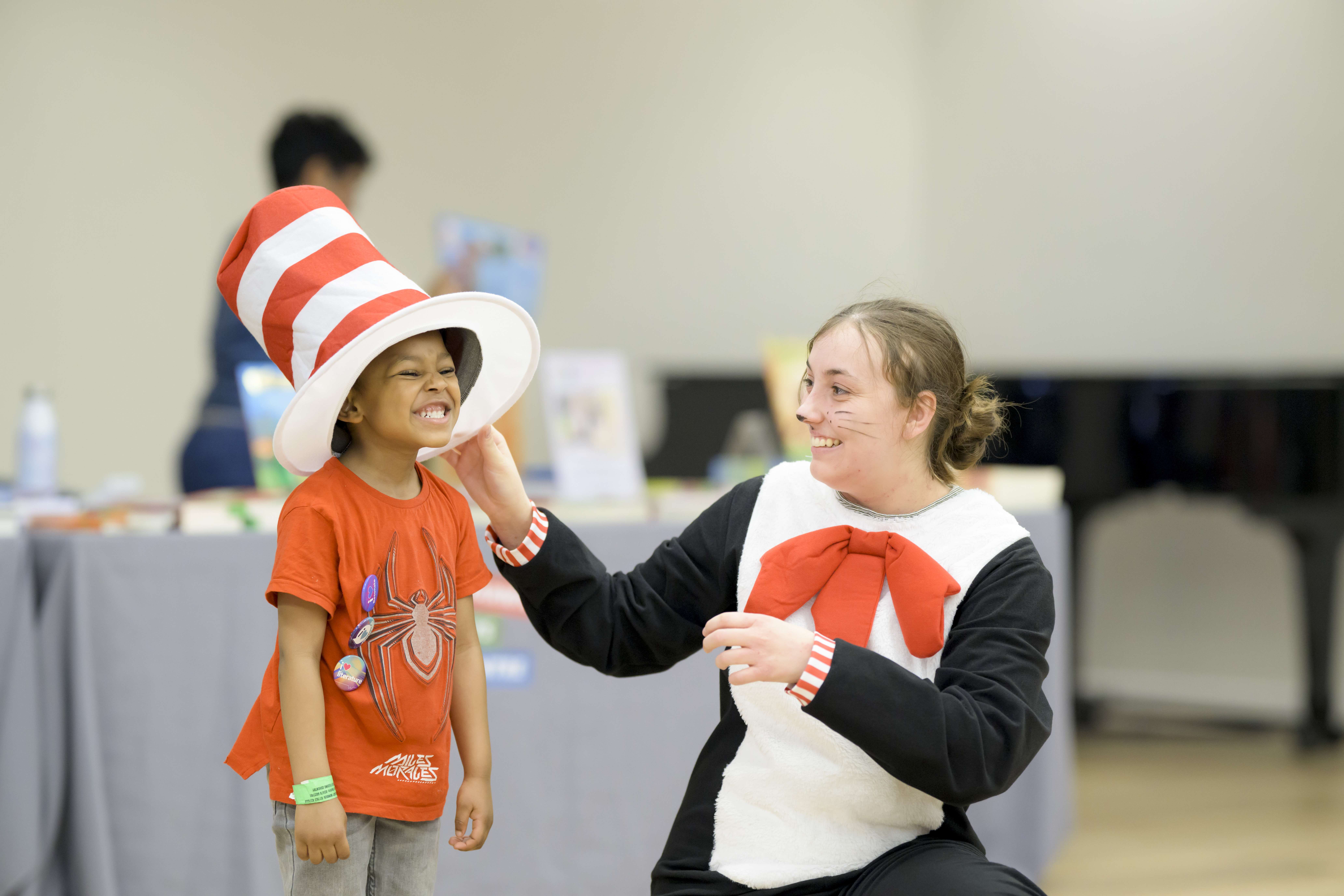 A women is dressed as the Cat in the Hat. She holds the hat on a young boys head, and he is grinning. 